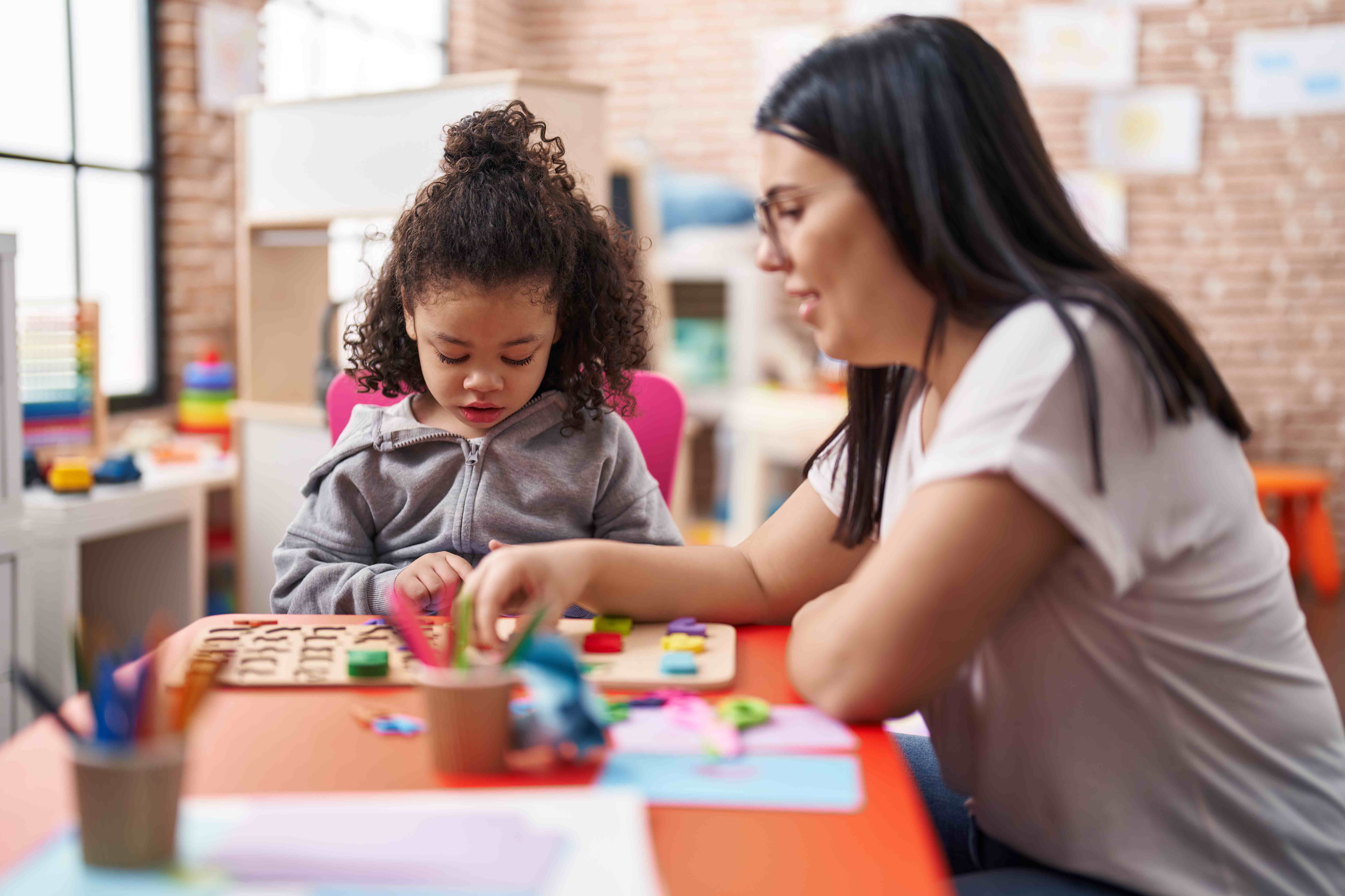 Maestra y niño pequeño jugando con rompecabezas de matemáticas en jardín de infantes